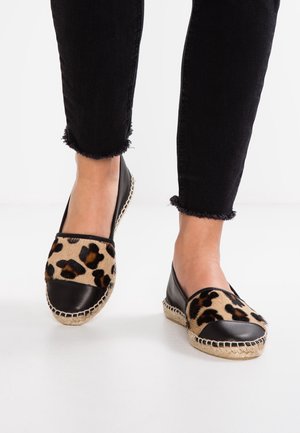 Feet wearing leopard print espadrilles with black toe caps and black frayed hem pants on a white floor.
