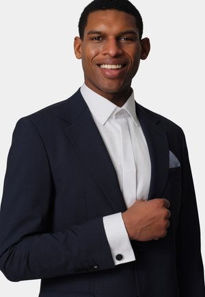 Navy suit jacket with a textured finish, white dress shirt, and contrasting cuff with black button detail. Pocket square features a check pattern.