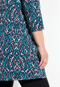 Korte mouw tuniek met een levendig, kleurrijk abstract patroon in blauw, roze en wit tegen een zwarte achtergrond. Zachte stof.