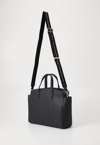 Sac à main en cuir noir avec une surface texturée, deux poignées et une bandoulière réglable avec un accent doré. Le design est structuré et rectangulaire.