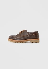 Brown leather lace-up shoe with a textured finish, cream-colored rubber sole, decorative stitching, and metal accents on the sides.