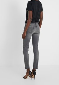 Szare dopasowane dżinsy z tylnymi kieszeniami i detalami w szwie, w zestawieniu z czarną dopasowaną bluzką i czarnymi sandałami na wysokim obcasie.