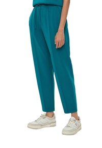 Teal joggers met elastische tailleband en trekkoord. Soepele stof met zijzakken. Gepaard met witte sneakers.