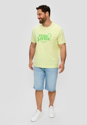 Lime green short-sleeve t-shirt with "PURE JUICE" graphic in green, paired with light denim shorts and white sneakers. Casual fit design.
