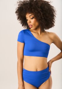 Blue one-shoulder bikini top with short sleeve and smooth texture; high-waisted bottom with gathered detail. Both made from stretchy material.