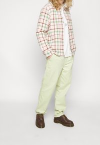 Checkered, pink, green, and brown flannel shirt over a white t-shirt; light green pants; brown lace-up boots with yellow stitching.