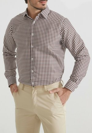 Chemise à carreaux marron et blanc avec un col pointu, des manches longues et une coupe ajustée, associée à un pantalon beige clair.