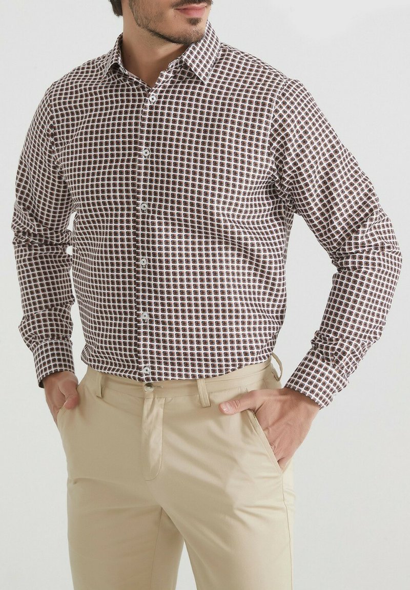 Chemise à carreaux marron et blanc avec un col pointu, des manches longues et une coupe ajustée, associée à un pantalon beige clair.