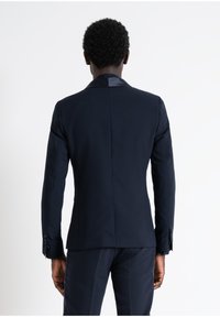 Giacca da uomo blu fatta di tessuto liscio, con colletto in satin, spalle strutturate e polsini con bottoni, vista dal retro.