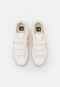 Zapatillas blancas con parte superior de cuero texturizado, tres correas de Velcro y acentos beige a los lados. Logo visible en la lengüeta.