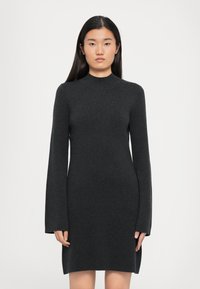 Feszes fekete kötött ruha hosszú ujjakkal, magas nyakkivágással és oldalsó hasítékokkal, sima textúrával és minimális dizájnnal.