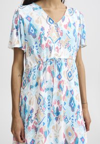 Kurzärmliges, V-Ausschnitt-Kleid aus einem leichten, strukturierten Stoff mit einem abstrakten Muster in Blau, Pink und Beige, das einen Bindegürtel in der Taille hat.