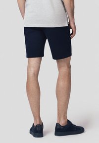 Granatowe bawełniane szorty o prostym kroju, w zestawieniu z ciemnymi trampkami. Widoczne przeszycia na końcu nogawek oraz boczne kieszenie.