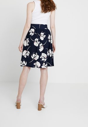 Jupe imprimée florale en tissu bleu marine, présentant des fleurs blanches et des accents verts, coupe mi-longue avec une taille froncée et une forme évasée.