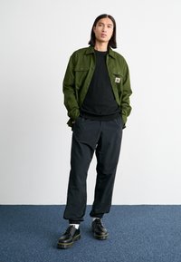 Green button-up shirt, black crew-neck t-shirt, black elastic-cuff pants, and black lace-up boots with yellow sole accents.
