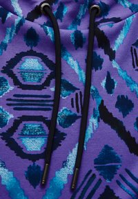 Lila Sweatshirt mit abstrakten blauen und schwarzen Mustern, schwarz gefärbten Kordeln und metallischen Akzenten an den Spitzen. Glatte Textur.