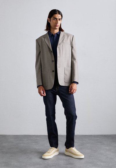 Heled hall blazer, mille krae, kaks eesmist taskut, tumesinine polo särk, tume teksapükk ja beežid sneakersid tekstuurse tallaga.