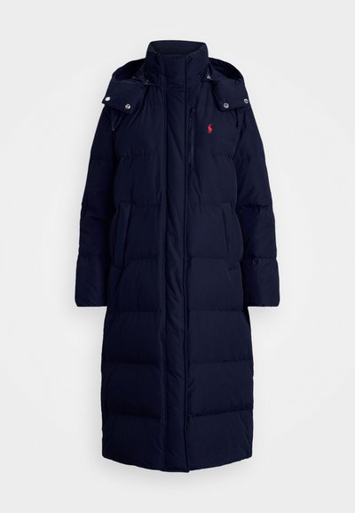 Laivastonsininen puhvitakki, jossa on korkea kaulus, etuvetoketju ja napit, kaksi sivutaskua ja pieni logokoriste rinnassa.