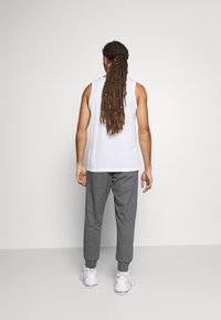 Vit ärmlös tanktopp och grå sweatpants med elastiska muddar, kombinerat med vita sneakers; bakifrån visas långt hår stylat i dreads.