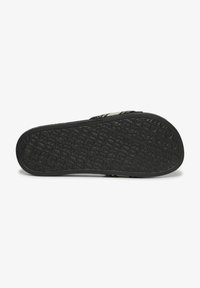 Suela de sandalia de goma negra con patrón texturizado, mostrando el nombre de la marca y detalles de diseño. Forma plana y ligeramente curvada, adecuada para el uso casual.