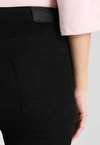 Svarta denimbyxor med en texturerad yta, med en framficka och en liten logotyp vid midjan.