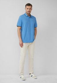 Lichtblauwe polo met korte mouwen en een kraag, gecombineerd met crèmekleurige broek en witte sneakers met grijze accenten.