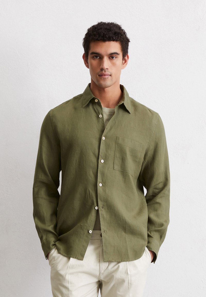 Olive green, long-sleeve linen shirt with a button-down collar, single chest pocket, and white buttons, styled with light beige pants.