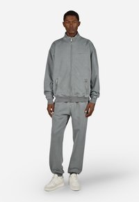 Pilka užtrauktuko striukė ir atitinkantys džinsai, pagaminti iš minkštos medžiagos. Yra įdėti nėriniai ant riešų ir šoninės užtrauktuko kišenės, derinama su baltais sportbačiais.