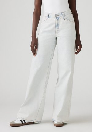 Light blue wide-leg jeans made of denim with a high waist and visible stitching. Paired with gray and white sneakers.