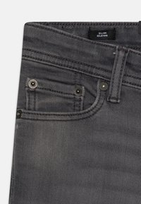 Sieviešu slim stila pelēkie džinsi ar gludu denim tekstūru, elegantu dizainu, divām priekšējām kabatām un melnas metāla detaļas akcentiem.