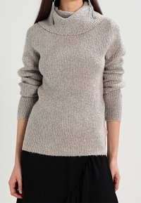 Šedý žebrovaný rolák s volným střihem a ohnutým límcem. Měkká textura, dlouhé rukávy a mírně zkrácený lem.