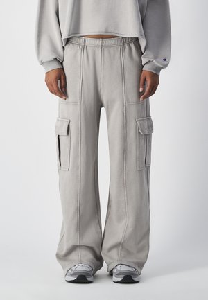 Lichtgrijze cargobroek met wijde pijpen, voorzien van gestikte details en twee grote zijzakken. Gecombineerd met grijze sneakers.