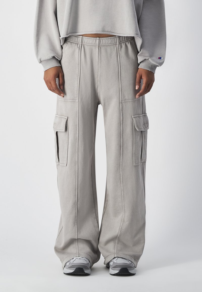 Lichtgrijze cargobroek met wijde pijpen, voorzien van gestikte details en twee grote zijzakken. Gecombineerd met grijze sneakers.