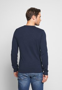 Pulover lung cu mânecă lungă de culoare bleu marin, fabricat dintr-un material moale, având un decolteu rotund și manșete și tiv cu țesătură în relief pentru un aspect ajustat.