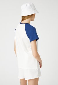 Bomull t-shirt med vit kropp och blå raglanärmar, ihopparad med vita shorts och en vit bucket hat. Enkel och avslappnad design.