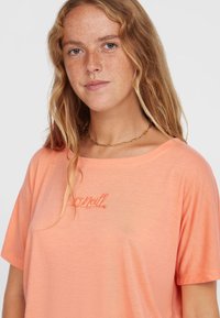 Korallenfarbener, lässig geschnittener T-Shirt mit kurzen Ärmeln und einer weichen Textur. Besitzt ein gesticktes Logo in einem helleren Farbton auf der Brust.