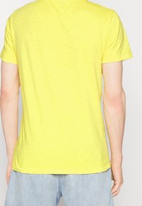 Keltainen lyhythihainen t-paita, jossa on teksturoitu pinta. Ominaisuuksiin kuuluu yksinkertainen pyöreä pääntie ja rento malli, joka sopii arkikäyttöön.