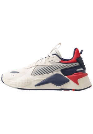 Low-top sneaker with white, navy, and red accents, textured fabric, thick sole, and lace-up closure in side profile on a white background.