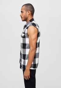 Fekete-fehér kockás, ujjatlan ing gombos elülső résszel és gallérral. Az anyag lágy és texturált hatású.