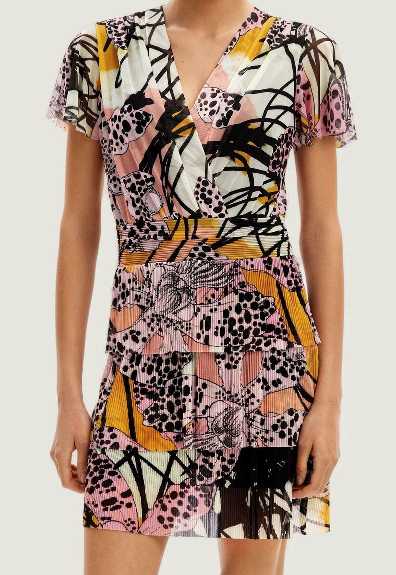 Femme portant une robe à manches courtes, col en V, jupe à volants et motif floral abstrait coloré en rose, jaune, noir et blanc.