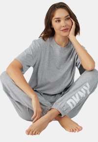 Grijze katoenen lounge-outfit met een relaxte t-shirt en taps tolopende broeken met elastische boorden. De broeken hebben een groot wit logo-detail.