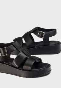 Sandalias de plataforma de cuero negro con múltiples correas anchas, detalles de hebilla plateada y una suela de goma texturizada para agarre.