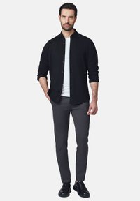 Czarna koszula z guzikami noszona na białym T-shircie, zestawiona z szarymi spodniami i czarnymi trampkami, o slim fit i gładkiej teksturze.