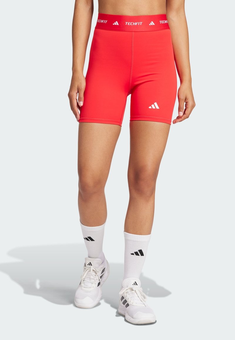Czerwone spodenki sportowe wykonane z elastycznego materiału, charakteryzujące się dopasowanym krojem, kontrastowym białym logo Adidas oraz brandingiem Techfit na talii.