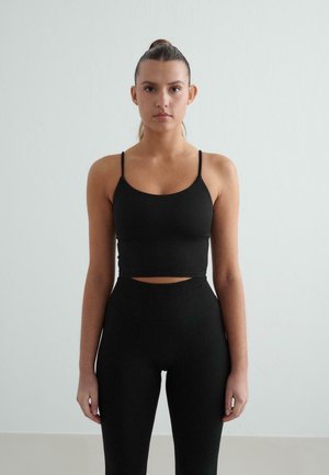 Top court noir à bretelles fines, associé à un legging noir taille haute, ajusté. Texture lisse, sans motifs ni éléments visibles.