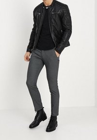 Svart läderjacka med dragkedjedetaljer, åtsittande svart t-shirt, grå skräddarsydda byxor och svarta snörkängor, som skapar en elegant, modern look.