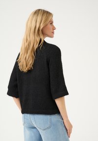 Schwarzer, gestrickter Pullover mit Dreiviertelärmeln, strukturiertem Finish und lässiger Passform, kombiniert mit hellblauen Jeans.