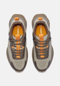 Bruine en grijze sneakers met een gestructureerde bovenkant, oranje accenten en stevige veters. Kenmerkt zich door een gevoerde kraag en een rubberen zool voor grip.