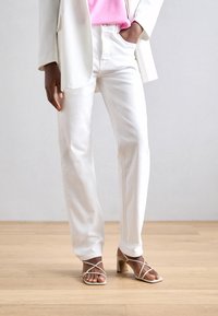 Pantalones de mezclilla blancos con corte recto, combinados con sandalias de tacón con tiras en tono nude. El conjunto se complementa con una blusa y una chaqueta en rosa claro.