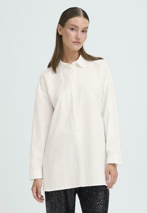 White button-up shirt with long sleeves, relaxed fit, and a classic collar. Textured fabric, lightweight, worn with sequined black pants.